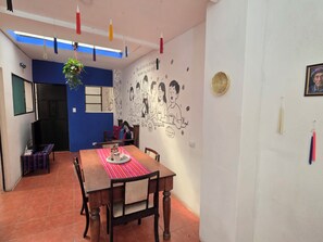 Un comedor con una mesa de madera, sillas, un mantel individual a rayas rojas y un mural en la pared.