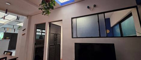 Una habitación con televisión, una planta colgante, una ventana y una puerta que da a otra estancia.