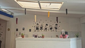 Un área de recepción con un mostrador blanco, un tragaluz y un mural que representa a baristas.