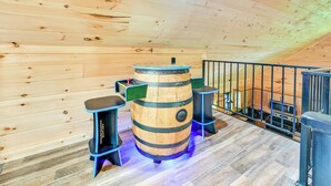 Une table en bois, en forme de tonneau, avec des tabourets, une rambarde et un coin cuisine à l’arrière-plan.