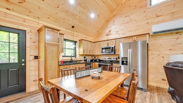 L’intérieur d’un chalet en bois comprend une table à manger, des chaises, une cuisine équipée et une porte noire.