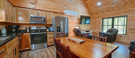 A wooden cabin interior with a kitchen, dining area, and seating.