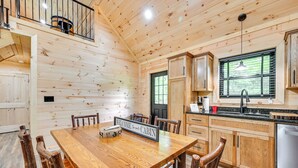 L’intérieur d’une cabane comprend une table à manger en bois, des chaises, une cuisine avec des meubles en bois et une fenêtre avec des stores.