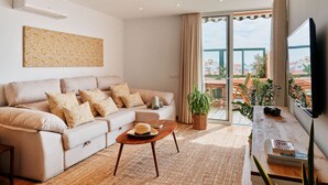 Una sala de estar con un sofá, una mesa de centro, un televisor de pantalla plana y un ventanal con vistas al exterior.