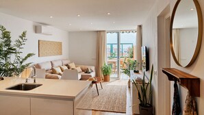 Una cocina moderna con una isla central, un comedor con sofá y sillas, y una sala de estar con televisor.