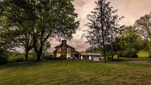 Ein Haus mit einem Steinkamin, umgeben von Bäumen und einem grünen Rasen.