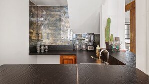 A modern kitchen with a black countertop, a backsplash with a marbled design, and a sink. There are various kitchen items on the counter, including a blender, a coffee maker, and glassware.