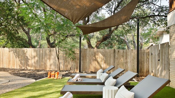 A backyard with a wooden fence, a shaded area with lounge chairs, and a well-maintained lawn.