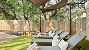 Un patio trasero con cerca de madera, un área sombreada con sillas de descanso y un césped bien cuidado.