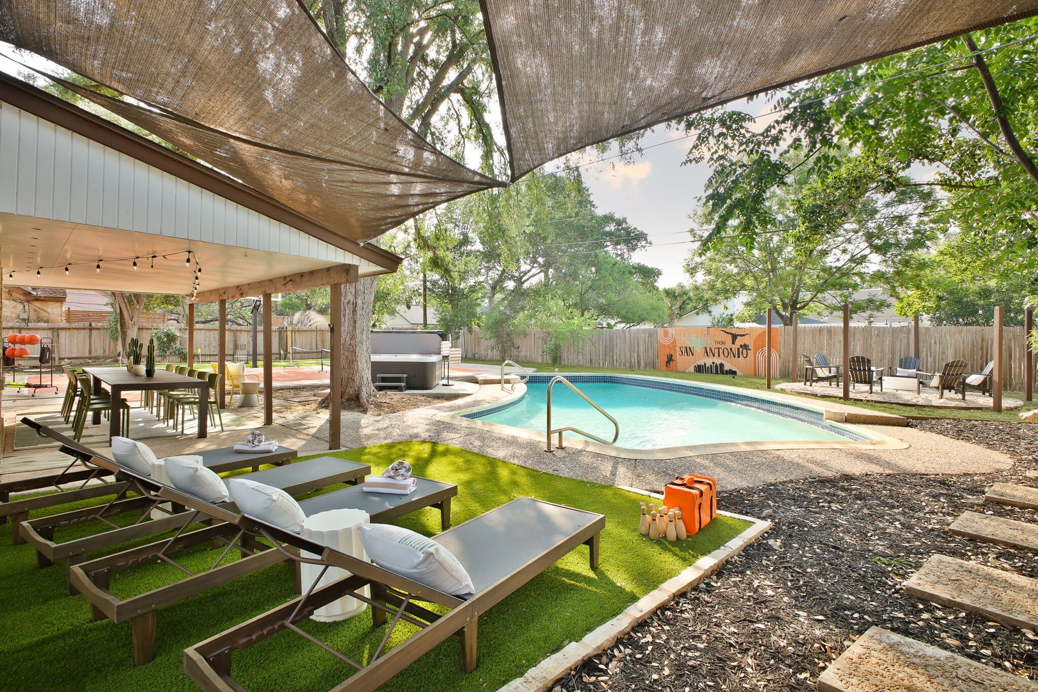 Un patio trasero con piscina, sillas de descanso, un porche cubierto y una cerca de madera.