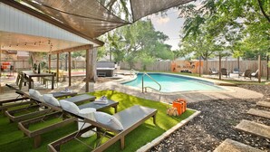 A backyard with a pool, lounge chairs, a covered patio, and a wooden fence.