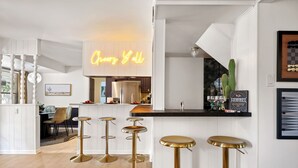 A modern kitchen with a neon sign, white cabinetry, and a bar area with stools.