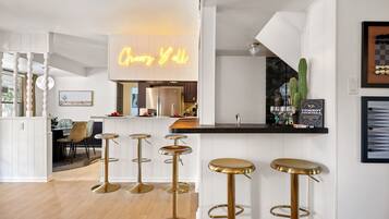 Cozinha moderna com um letreiro de neon, armários brancos e um espaço de bar com banquetas.