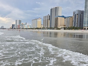 A beach with waves and a city skyline in the background.