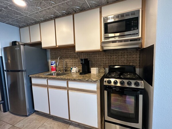 A kitchen with white cabinets, a stainless steel refrigerator, a microwave, a stove, and a sink. - Low Tide Loft/Premium Location (Myrtle Beach)