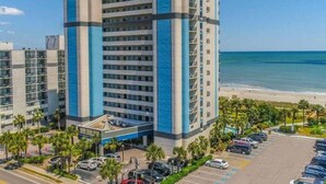 A multi-story hotel with a modern design, located near a beach with a parking lot and palm trees. - Boardwalk Breeze! Premium Location (Myrtle Beach)