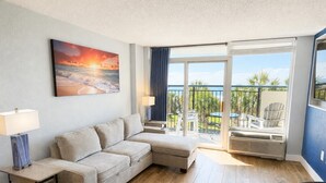 A living room with a sofa, a lamp, a painting, and a view of the outdoors. - Boardwalk Breeze! Premium Location (Myrtle Beach)