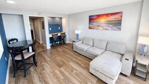 A modern living room with a sofa, a dining table with chairs, and a painting on the wall. - Boardwalk Breeze! Premium Location (Myrtle Beach)