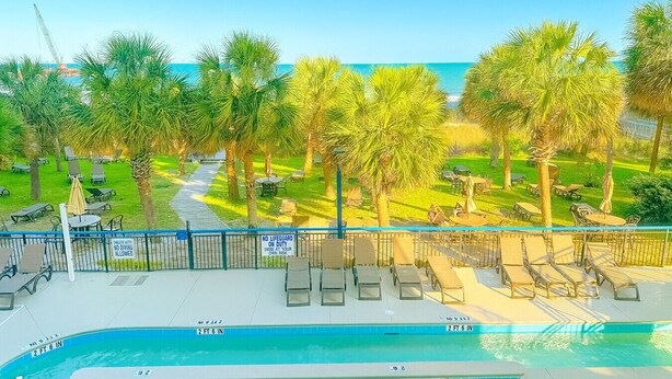 A poolside area with lounge chairs, a sign indicating no lifeguard on duty, and a view of the ocean. - Boardwalk Breeze! Premium Location (Myrtle Beach)