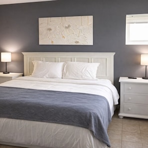 Un dormitorio con una cama, dos mesitas de noche, una lámpara de pared y un adorno sobre la cama.