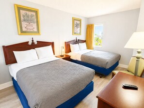 A hotel room with two beds, a small table, a lamp, and a window with curtains. - Wake up to the waves (Myrtle Beach)