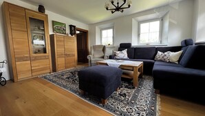 Una sala de estar con sofá, reposapiés, mueble de madera y alfombra estampada.