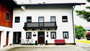 Un edificio blanco con detalles de madera, un balcón y un banco rojo en el exterior.