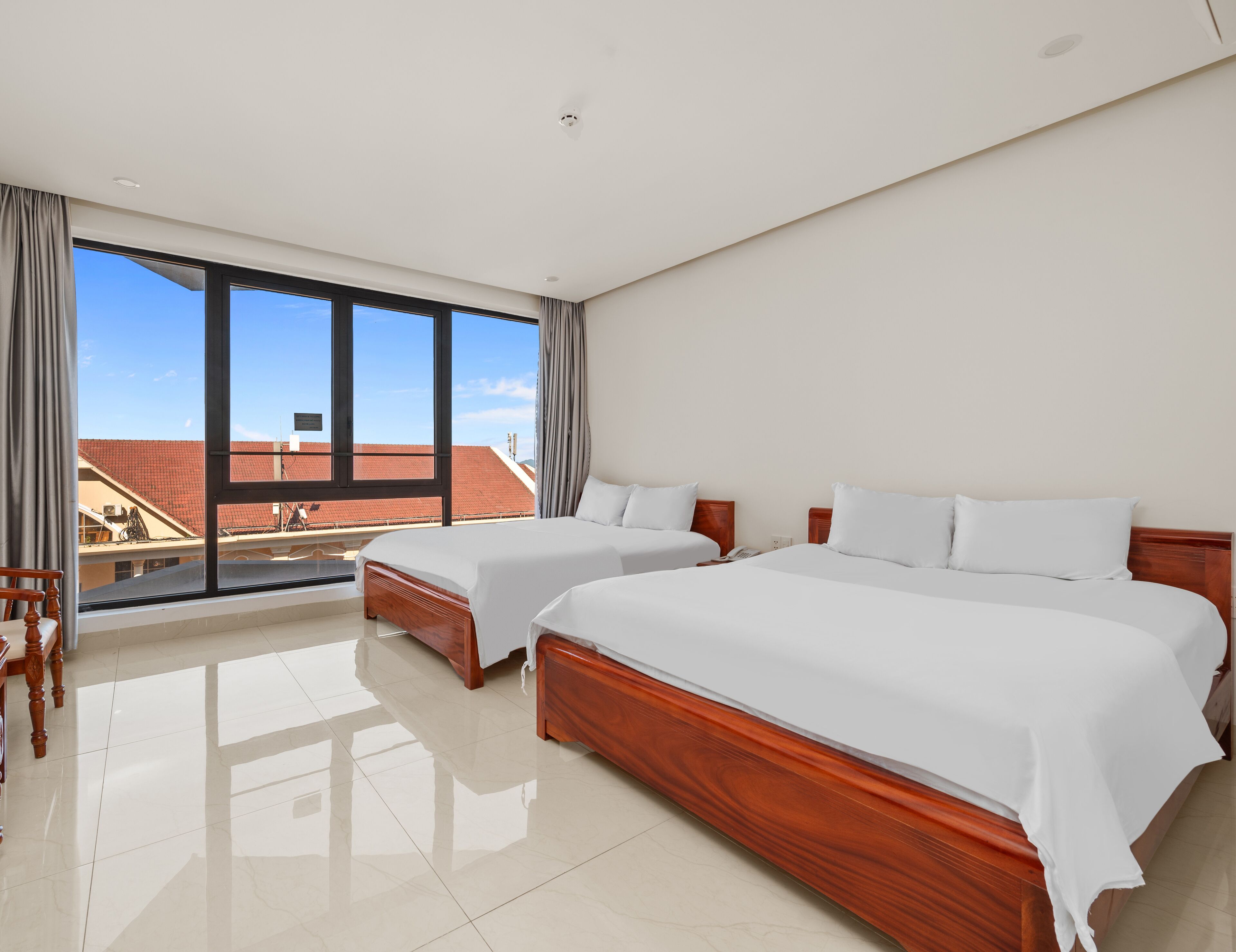 Ein Hotelzimmer mit zwei Betten, einem großen Fenster und Blick auf Gebäude.