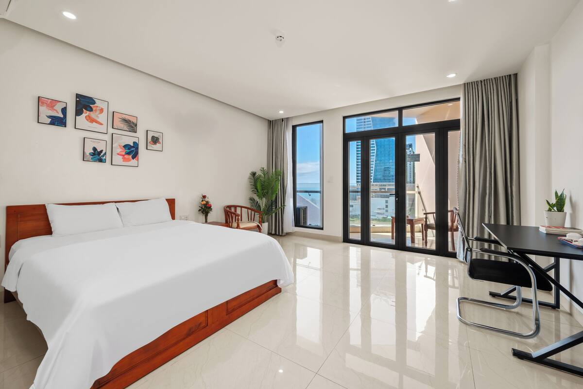 Una camera d'albergo moderna con un letto grande, una scrivania e un balcone vista città.