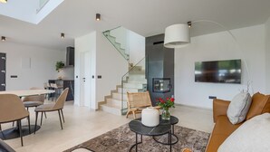 A modern living room with a staircase, a dining area, and a TV mounted on the wall.