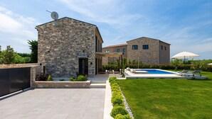 A two-story stone house with a swimming pool, outdoor seating, and a well-maintained lawn.