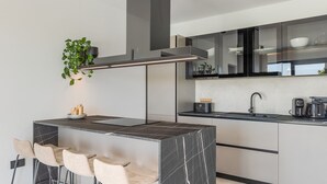 A modern kitchen with a marble island, bar stools, a coffee machine, and a hanging plant.