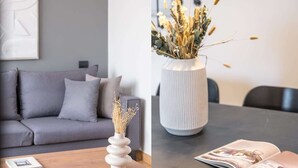En moderne stue med en grå sofa, et træbord og en hvid vase med tørrede planter.