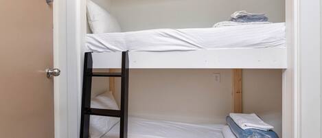 A bunk bed room with a ladder, white bedding, and a sign on the door.