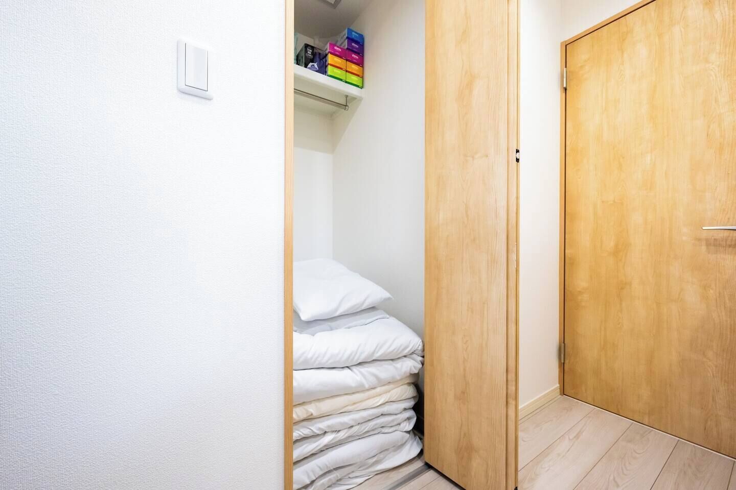 A narrow hallway with a wooden door on the right and a stack of white bedding on the left.