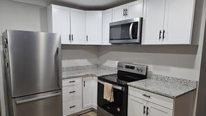 A kitchen with white cabinets, a stainless steel refrigerator, a microwave, and a black oven.
