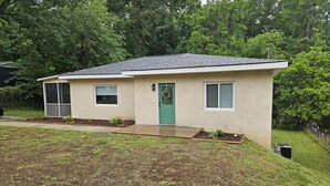 A single-story house with a green door, a small porch, and a front yard with a garden bed.