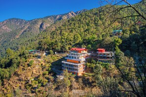 Un hotel de varios pisos con balcones, situado en una zona montañosa con un bosque denso.