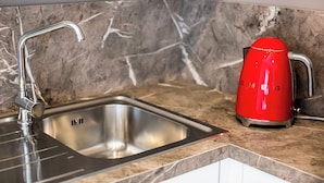 A kitchen with a stainless steel sink, a red kettle, and a marble backsplash. - Benzi16 (Como)