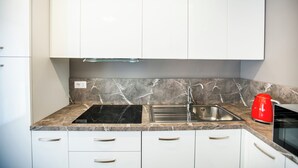A modern kitchen with white cabinets, a marble countertop, a black stovetop, a stainless steel sink, and a red kettle. - Benzi16 (Como)
