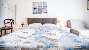 A neatly made bed with a blue and white patterned bedspread, two folded towels, a wooden chair, a nightstand with a lamp, and a framed picture on the wall. - Benzi16 (Como)