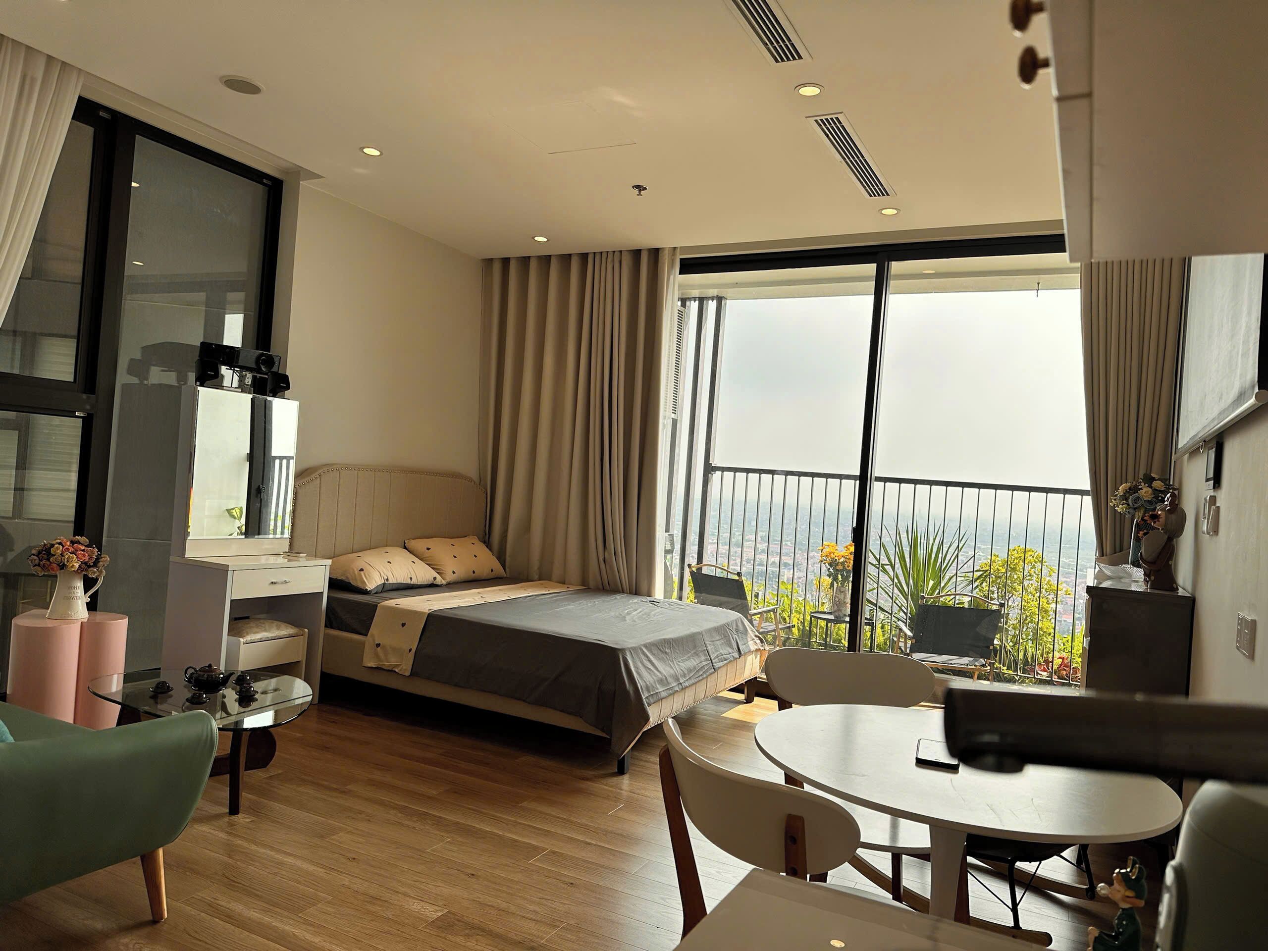 A modern hotel room with a bed, a desk, a chair, a round table, and a balcony with a view.
