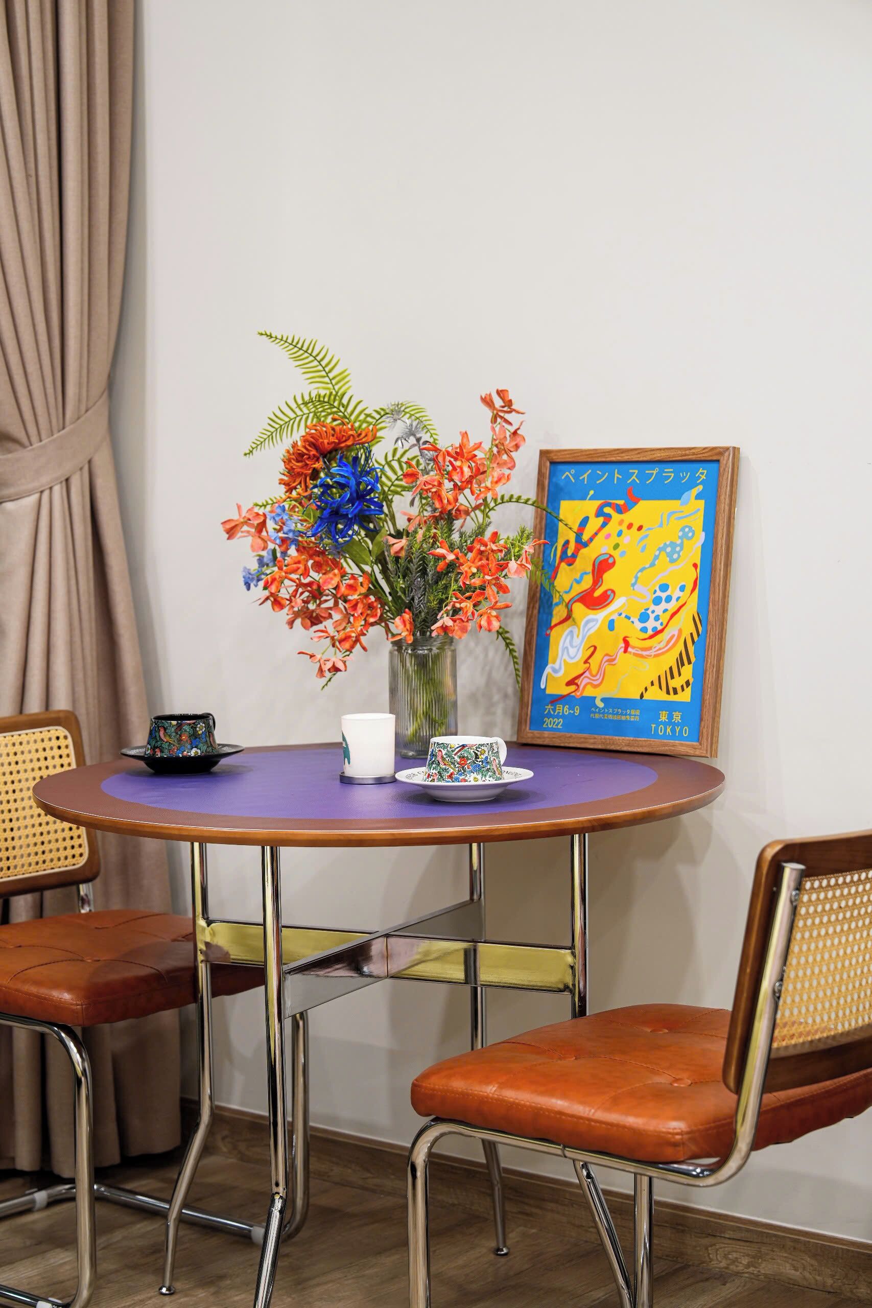 Een ronde tafel met een bloevas, een ingelijst kunstwerk en een klein bord met een kopje.