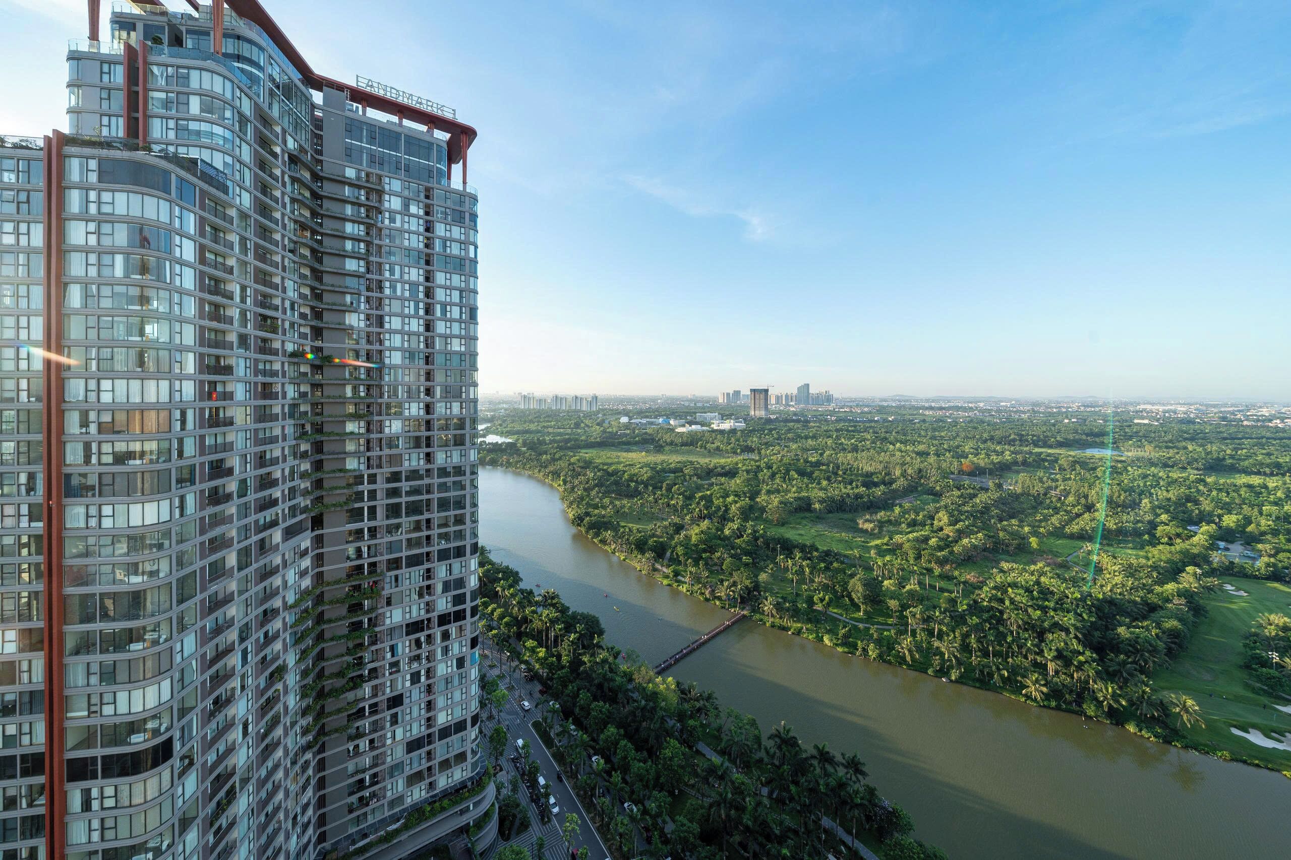 A high-rise building with a curved facade, a river in the foreground, and a distant cityscape.