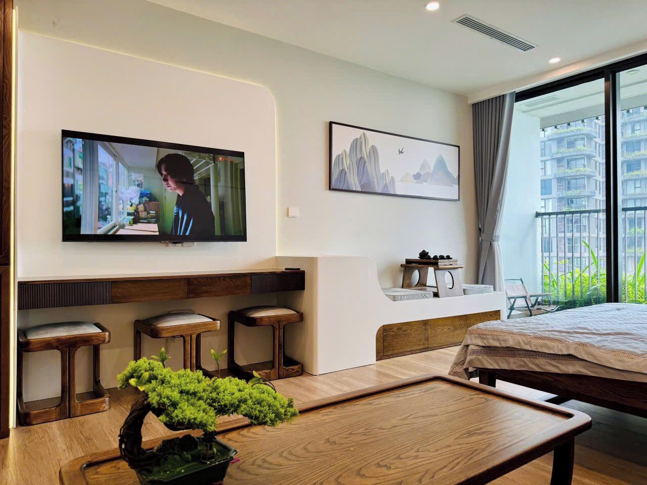 Ein modernes Hotelzimmer mit Bett, Wandfernseher, kleinem Schreibtisch und Fenster mit Stadtblick.