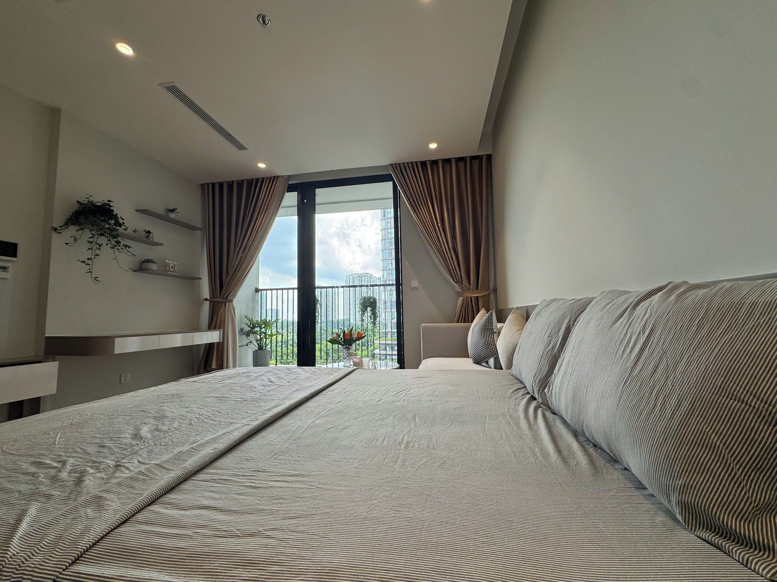 A modern bedroom with a large bed, a balcony with a view, and a small seating area.