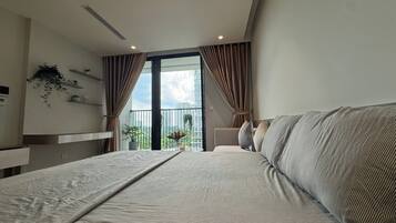A modern bedroom with a large bed, a balcony with a view, and a small seating area.