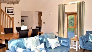 Uma sala de estar com sofá, cadeiras, uma mesa de jantar e uma janela com cortinas.
