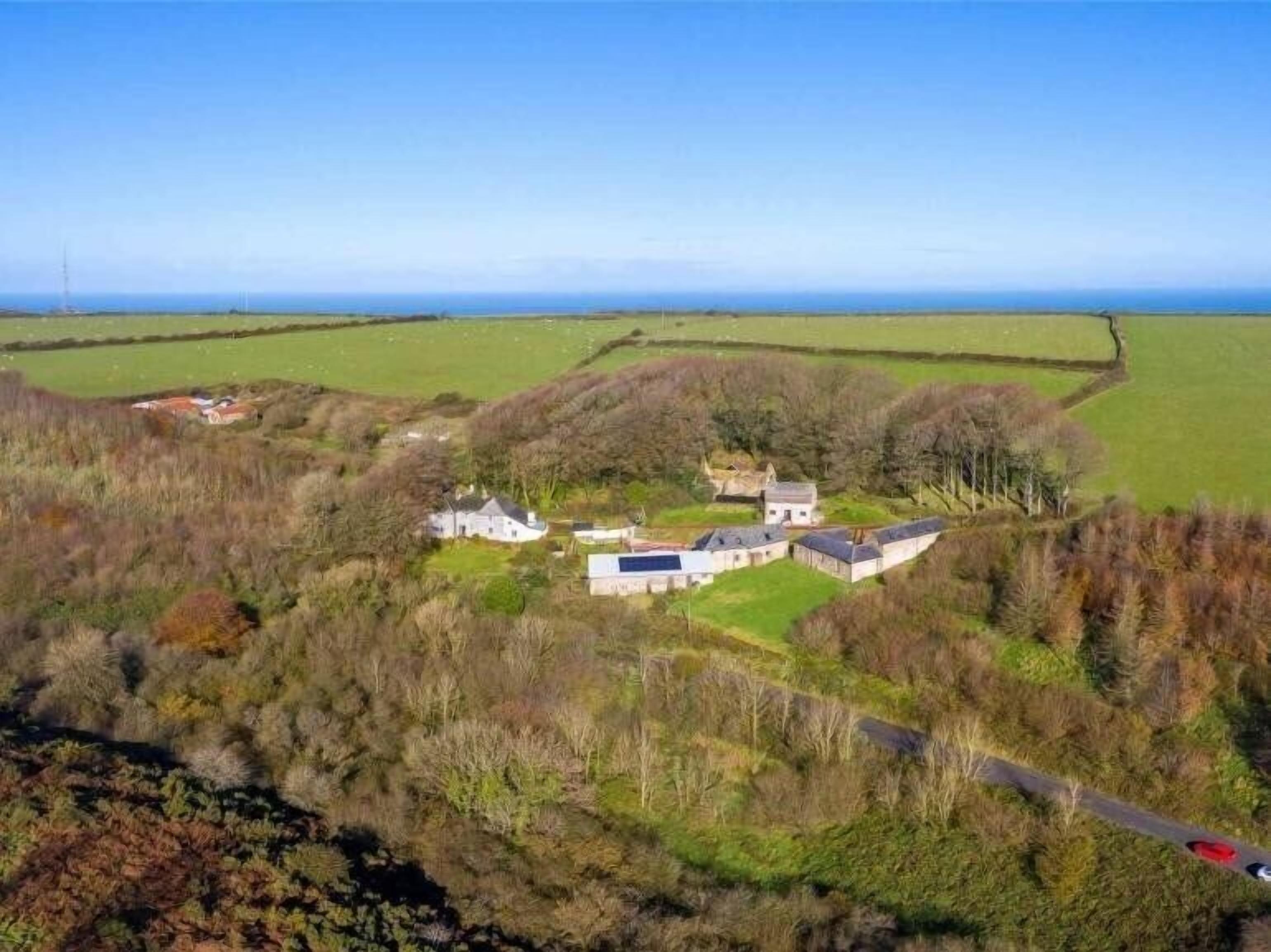 A rural property with multiple buildings, a road, and a view of the sea.