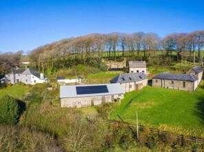 A rural property with multiple stone buildings, a fenced yard, and a hilly landscape in the background.
